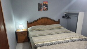 A bedroom with a wooden bed, a nightstand with a lamp, and a wall-mounted shelf.