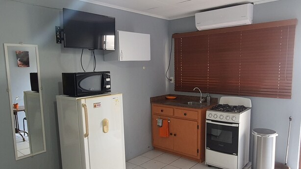 A compact kitchen with a refrigerator, microwave, stove, sink, and a small window with blinds.