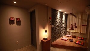 A room with a stone wall, a wooden platform with colorful cushions, and a small table with a lamp. - Hwon Guest House (Seoul)