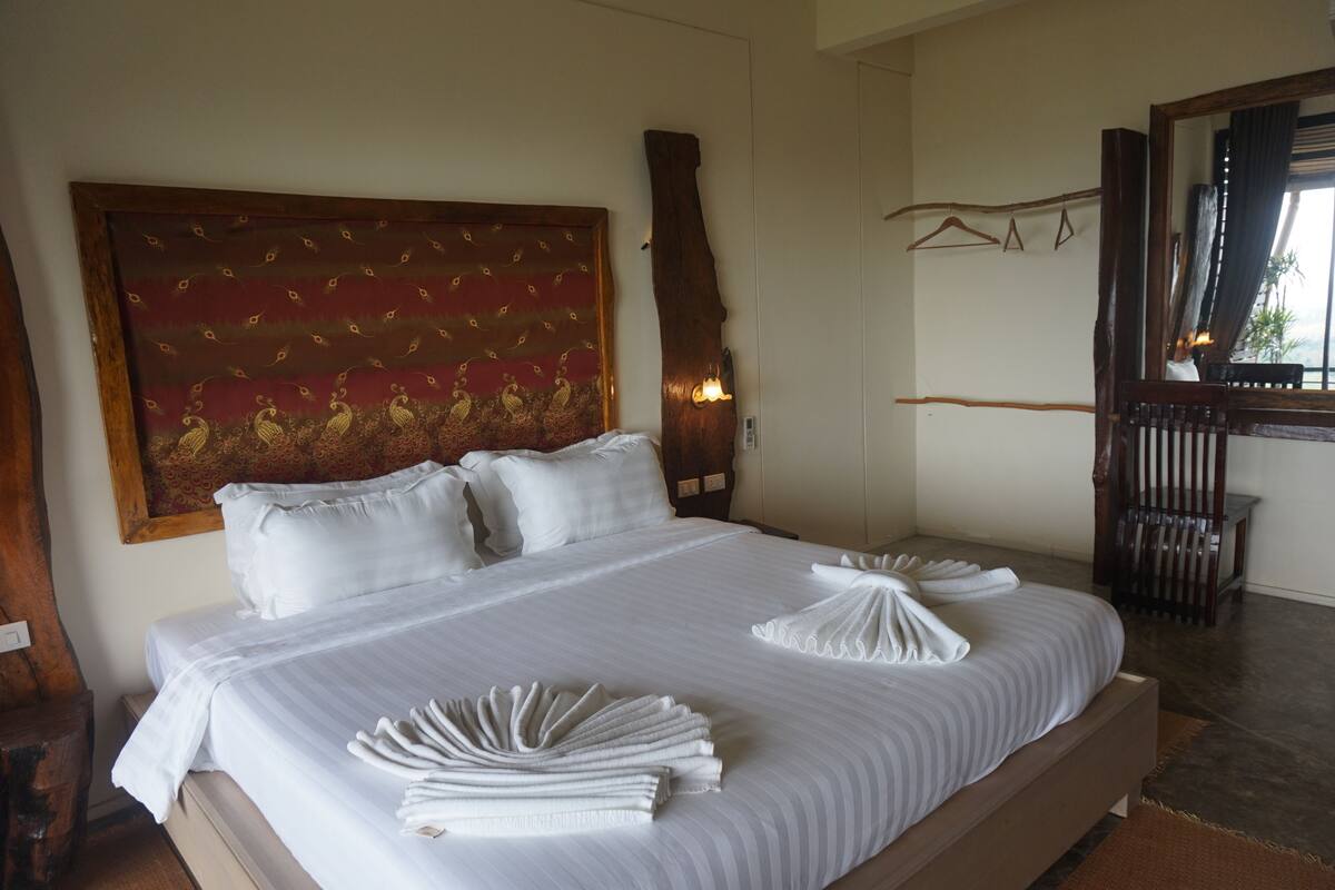 A neatly made bed with white linens and towels, a large decorative headboard, and a wooden bench in the corner.