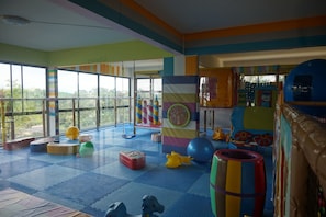A brightly colored indoor play area with a large window, play structures, and a blue mat floor. - The Adventure Mountain Club (Takua Thung)