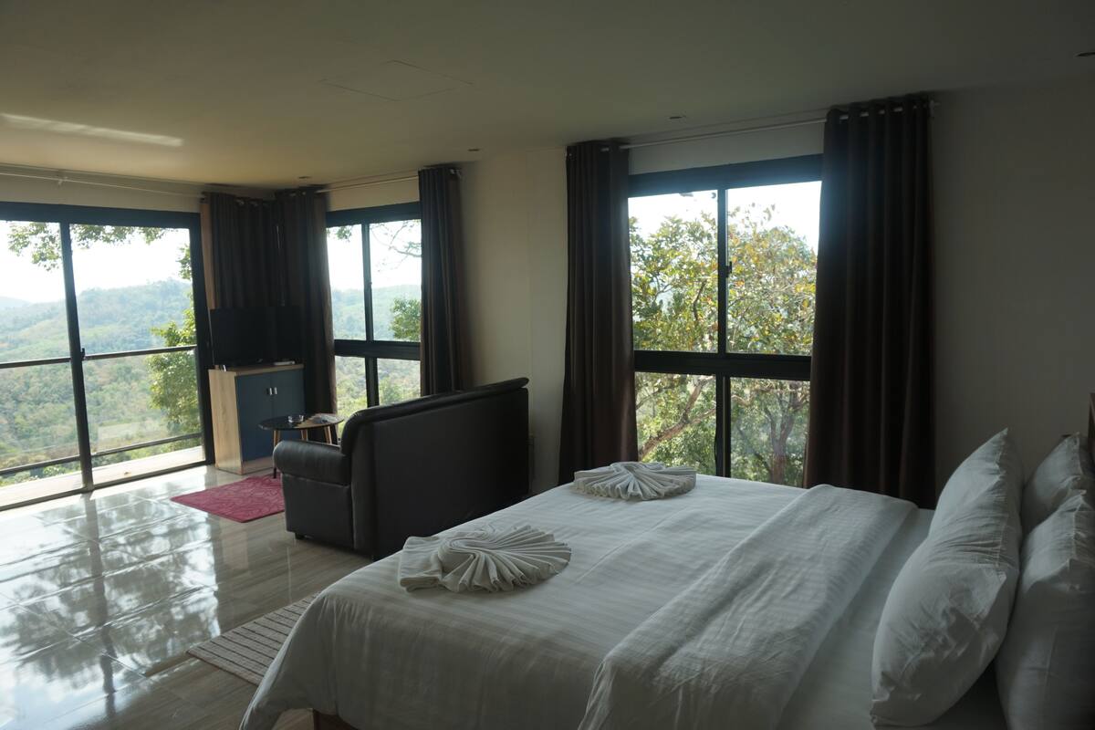 A modern hotel room with a large bed, a desk, and a view of the mountains.
