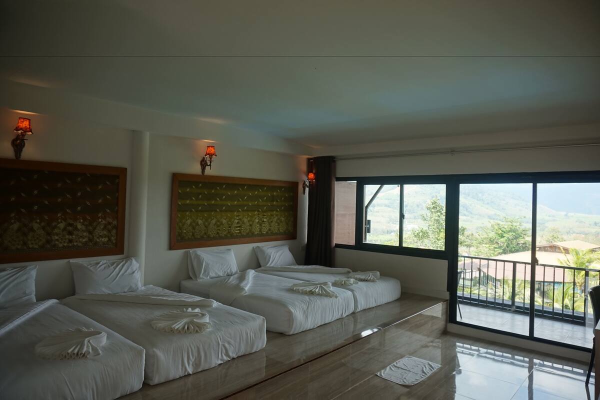 A hotel room with two beds, a large window with a view of the countryside, and wall-mounted lamps.