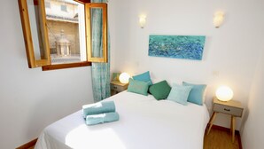 A bedroom with a bed, two bedside tables, a nightstand, a window with a view, and a painting on the wall. - Lovely and Central Apartment in Palma, Wifi, AC, Balcony, Fully Equipped & Cozy (Palma)