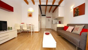 A modern living room with a white coffee table, a grey sofa with red cushions, a dining area with a white table and chairs, and a kitchen area with white cabinets and a microwave. - Lovely and Central Apartment in Palma, Wifi, AC, Balcony, Fully Equipped & Cozy (Palma)
