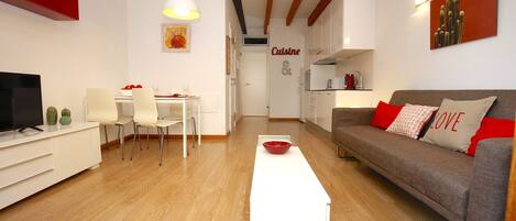 A modern living room with a dining area, a sofa with a 'LOVE' pillow, a TV, and a red bowl on a table.