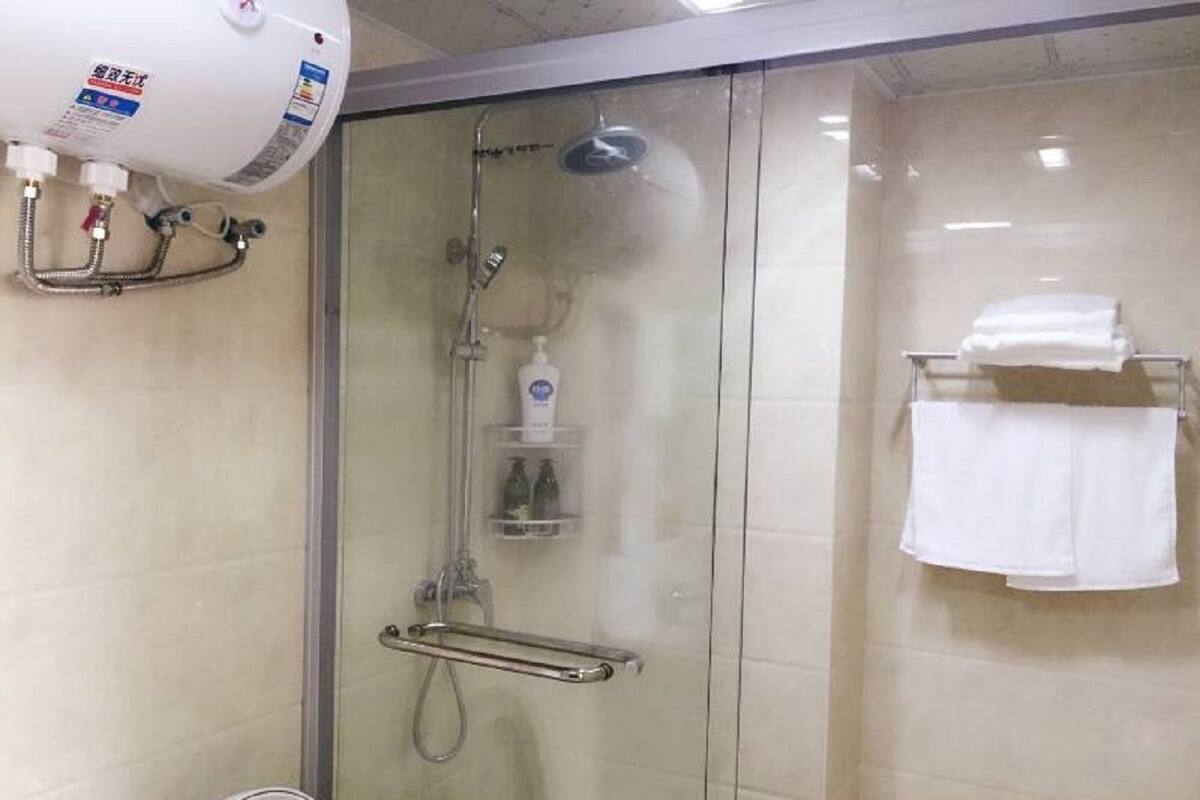 Cabina de ducha con paredes de vidrio, cabezal de ducha de mano, dispensador de jabón y toallero con toallas dobladas.