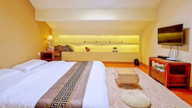 Habitación de hotel con una cama grande, televisión, mesita de noche, repisa con objetos decorativos y tragaluz.