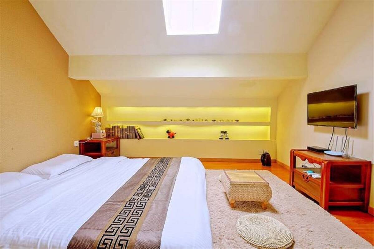 Habitación de hotel con una cama grande, televisión, mesita de noche, repisa con objetos decorativos y tragaluz.