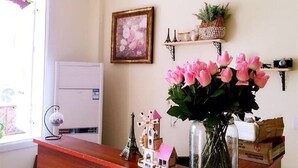 Una habitación con un escritorio de madera, un florero de flores rosas, un cuadro enmarcado y un estante con adornos.