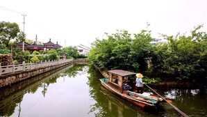 Una embarcación tradicional en un río tranquilo, rodeada de abundante vegetación y un edificio histórico al fondo.
