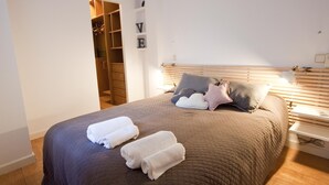Een net opgemaakt bed met twee opgerolde handdoeken, een houten hoofdbord en een nachtkastje met een lamp.