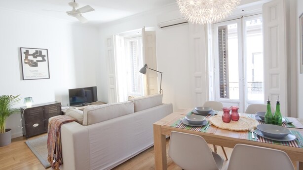 Een moderne woonkamer met een bank, een eettafel gedekt met borden en glazen, een televisie en een plafondventilator.
