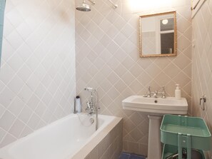 A bathroom with a bathtub, a sink, a mirror, and a green basket.