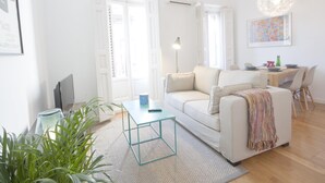 Een lichte woonkamer met een witte bank, een klein tafeltje en een eethoek met tafel en stoelen.