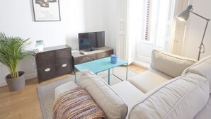 Een moderne woonkamer met een bank, een televisie, een salontafel en een potplant.