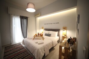 Una habitación de hotel moderna con una cama bien hecha, una mesita de noche con lámpara, aire acondicionado de pared y un ventanal con cortinas.