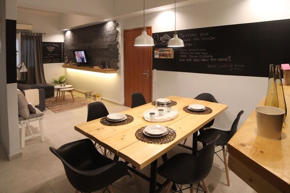 Un comedor moderno con una mesa de madera dispuesta para cuatro personas, sillas negras y una pizarra con escritura en la pared.