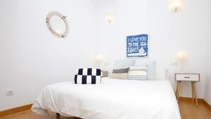 Un dormitorio con una cama blanca, almohadas a rayas, un letrero azul y una mesita de noche con una lámpara.