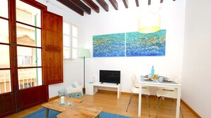 Una habitación con puerta de madera, televisor, escritorio y sillas, y dos cuadros en la pared.