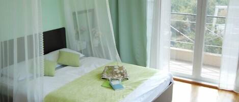 Une chambre à coucher avec un lit, une literie verte, un baldaquin et une vue sur la verdure à l’extérieur.