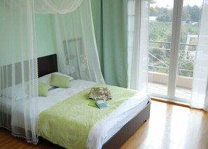 Ein Schlafzimmer mit Bett, grüner Bettwäsche, einem Baldachin und Blick auf Grünfläche draußen.