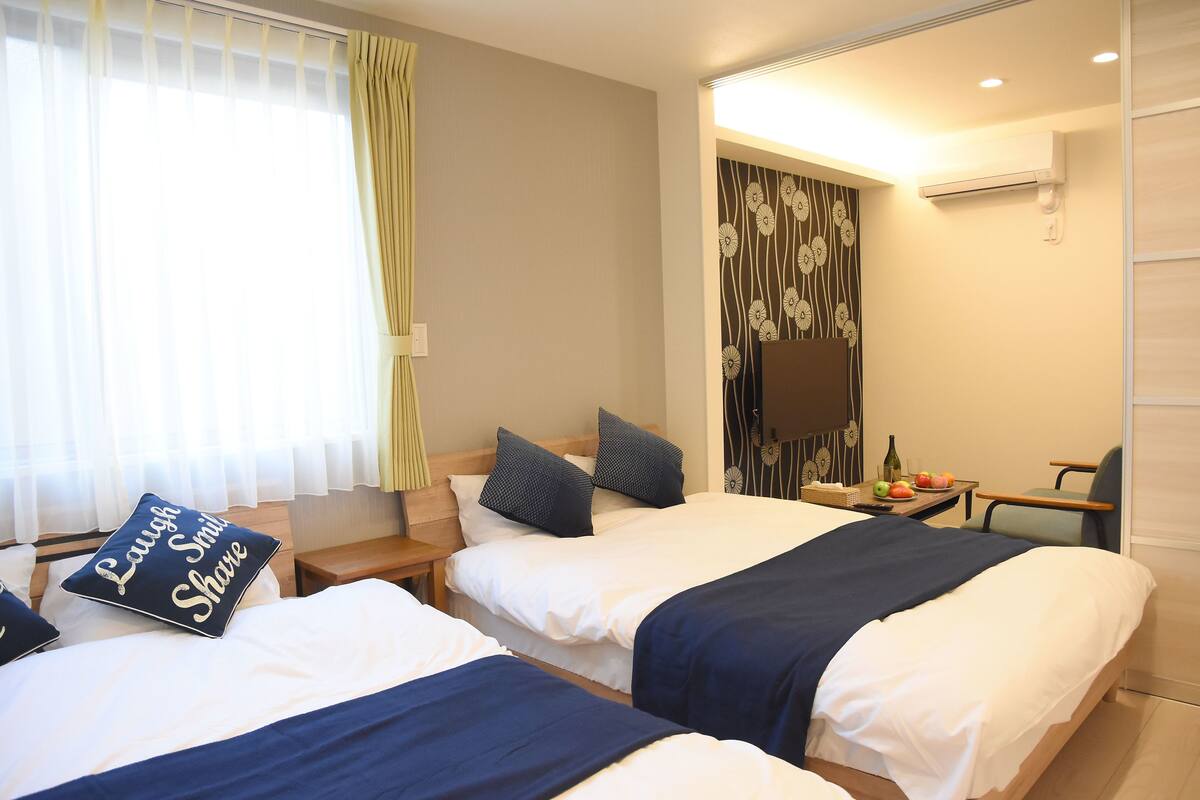 Une chambre d’hôtel avec deux lits, une petite table sur laquelle se trouvent une bouteille et des fruits, et une chaise.