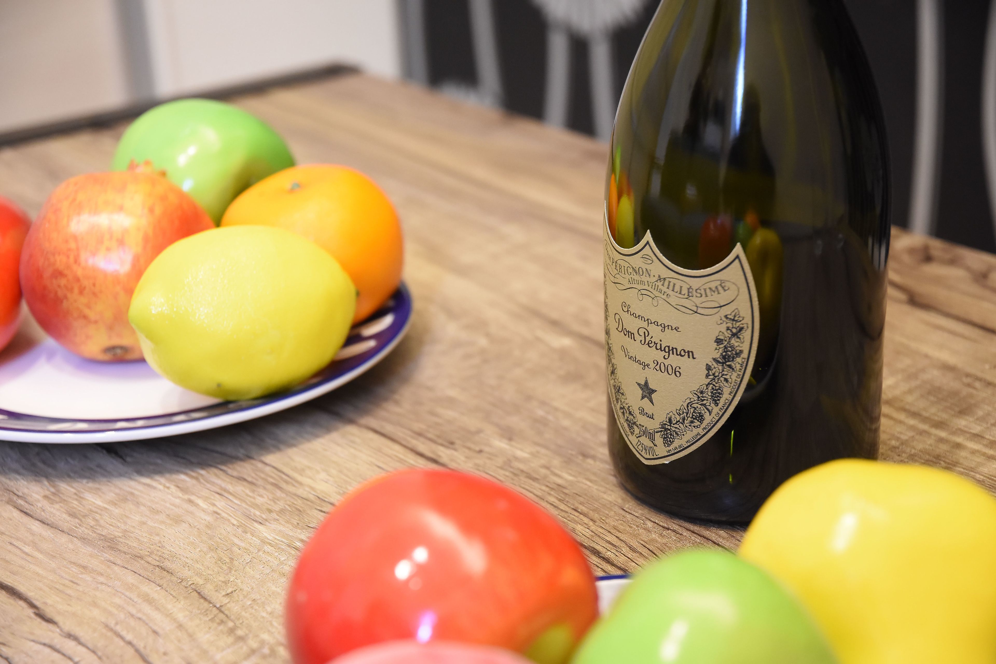 Une bouteille de champagne et une assiette de fruits sur une table en bois.