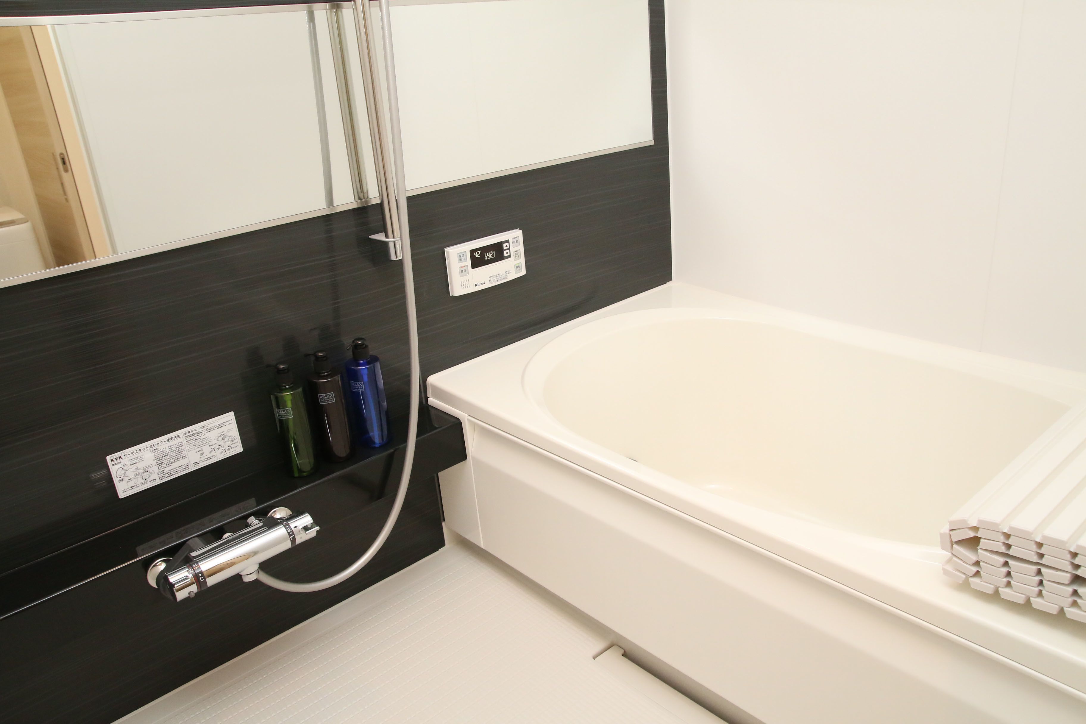 A modern bathroom with a bathtub, a mirror, and a control panel for the water heater.