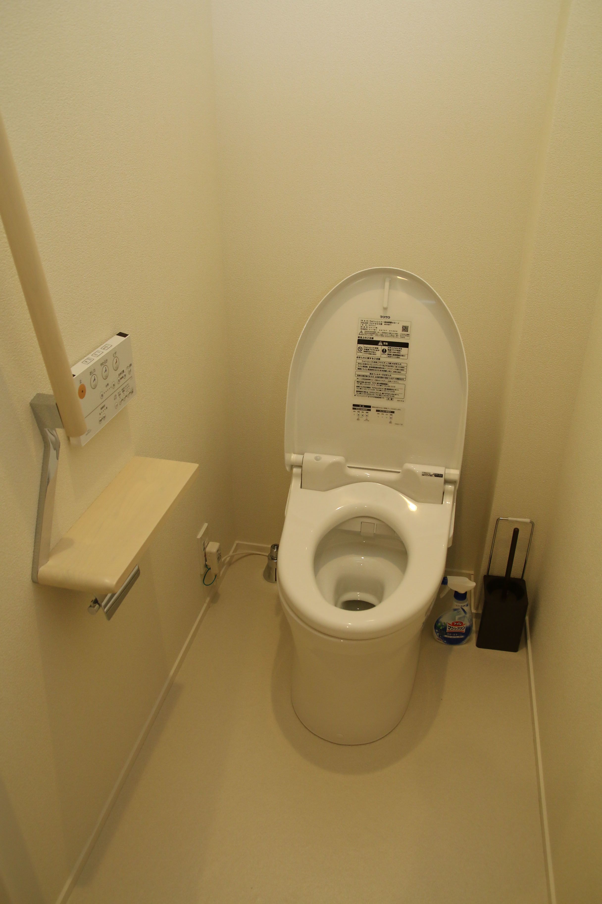 A small, white toilet with a closed lid, a wall-mounted flush handle, and a small shelf above it.