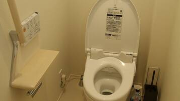 A small, white toilet with a closed lid, a wall-mounted flush handle, and a small shelf above it.