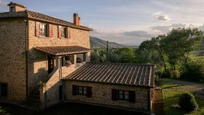Een gebouw van steen met een pannendak, een balkon en uitzicht op een bergachtig landschap.