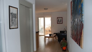 Amplia sala de estar con puerta de vidrio corredera a un balcón, un sofá negro, una mesa de centro de madera y una planta en maceta.