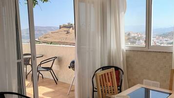 A room with a glass door leading to an outdoor area, a table with chairs, and a view of a hilly landscape.