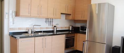 A modern kitchen with wooden cabinets, a stainless steel refrigerator, a built-in oven, and a microwave.