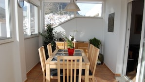 Un comedor con una mesa y sillas de madera, una planta en maceta y vistas a un pueblo a través de amplios ventanales.