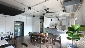 Uma sala de jantar espaçosa com uma mesa comprida e cadeiras, um ventilador de teto e uma planta em vaso.