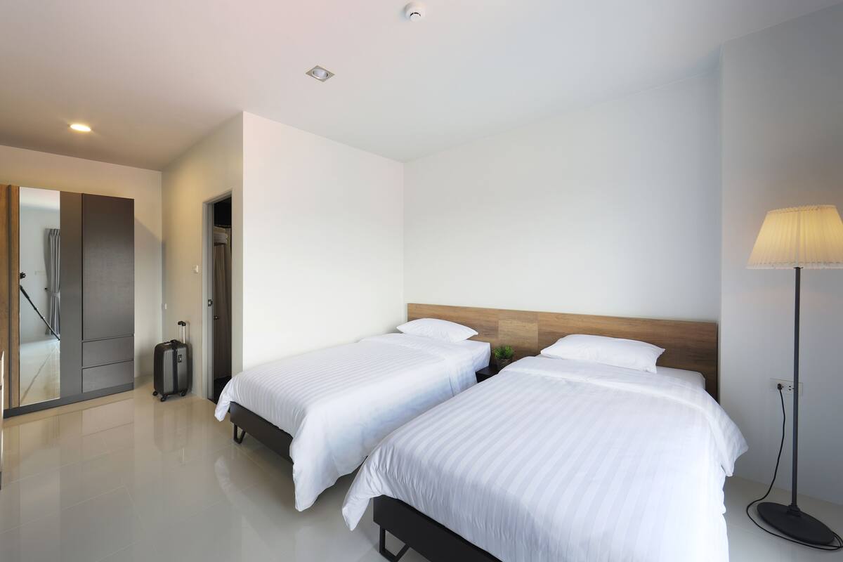 Una habitación de hotel moderna con dos camas, una mesita de noche, una lámpara y una maleta.