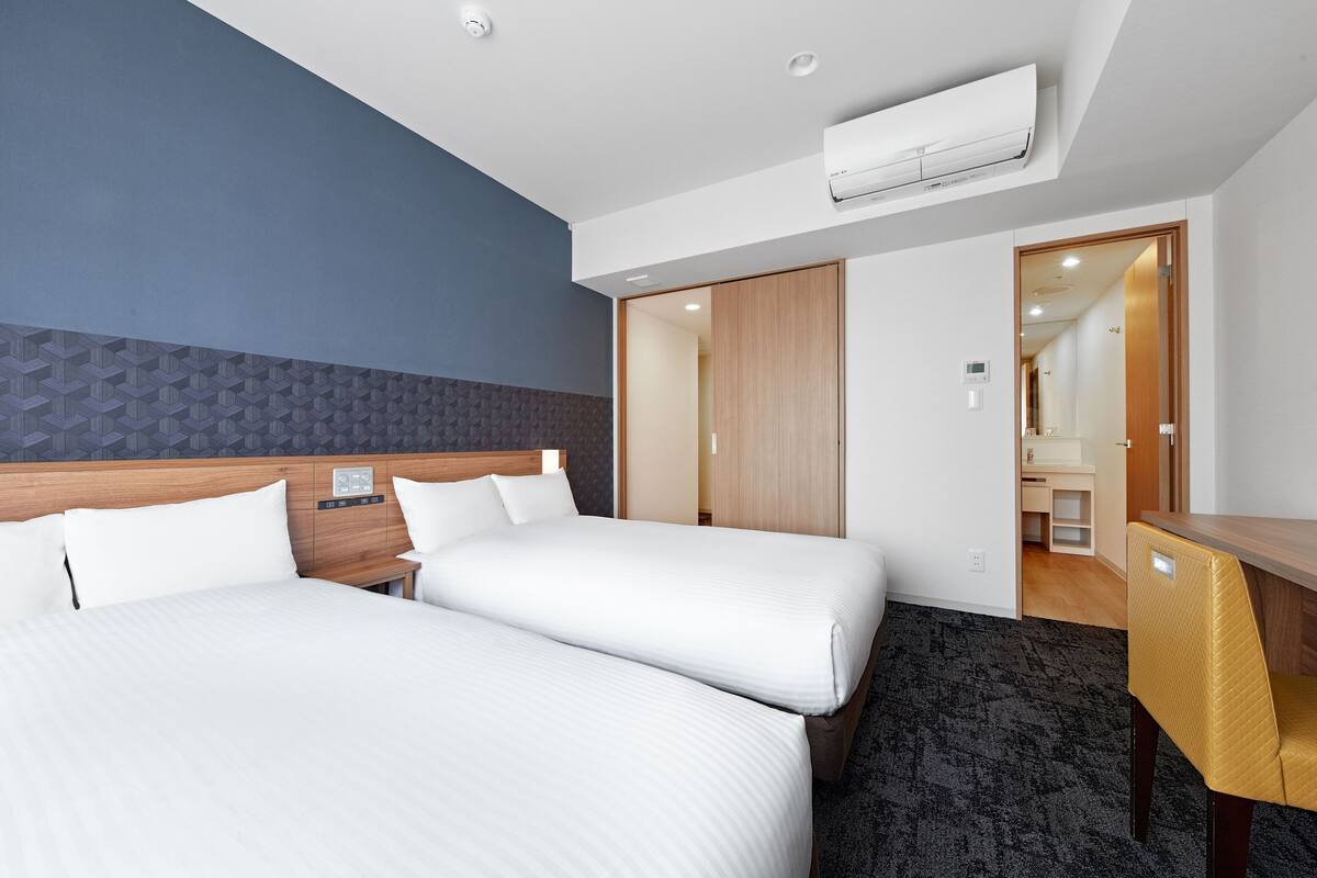 A hotel room with two beds, a wooden headboard, a desk, and an air conditioning unit.