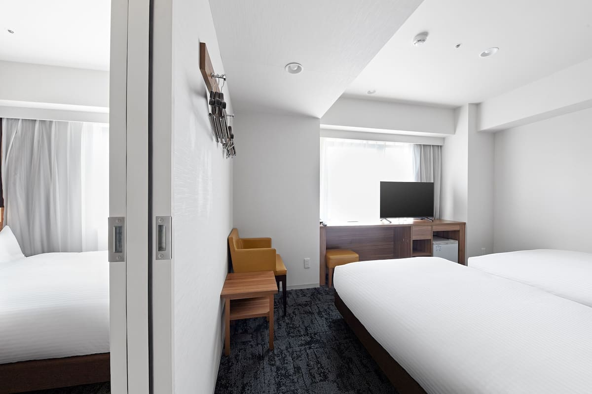 A hotel room with two beds, a desk, a chair, a television, and a window with curtains.