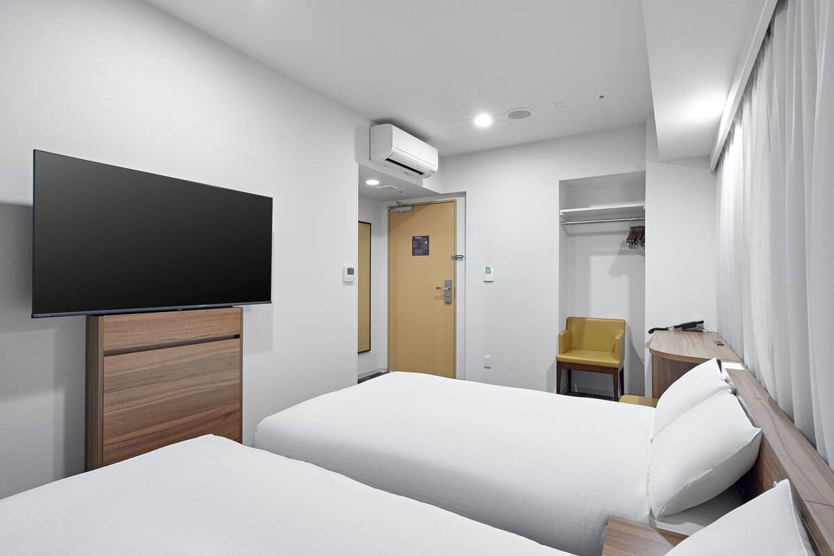 A hotel room with two beds, a flat-screen TV, a wooden headboard, a desk with a chair, and a wardrobe.