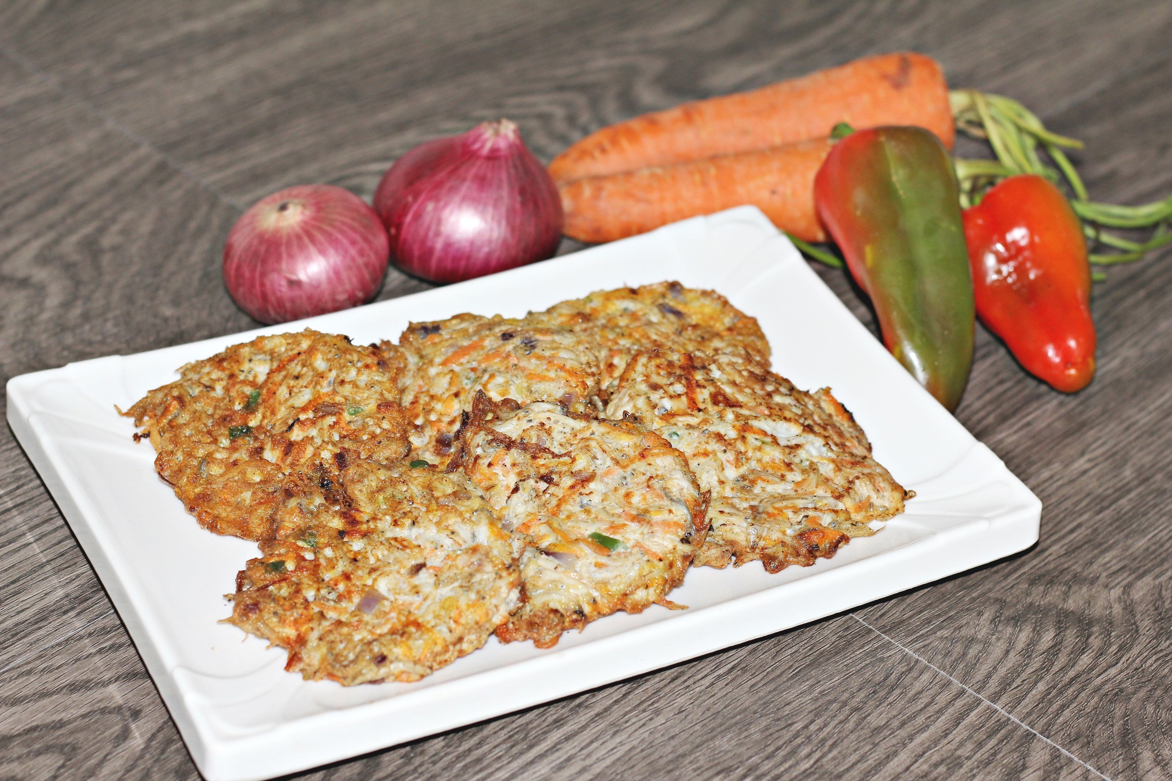 A plate of food with vegetables and a white plate on a wooden surface.