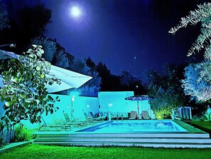 A nighttime outdoor pool area with lounge chairs and umbrellas, surrounded by trees and a mountain in the background. - SPECIAL OFFER Villa del Tilo (Huetor Santillán, Granada)