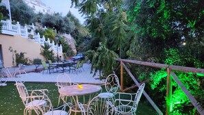 Eine Terrassengruppe im Freien mit weißen Metallstühlen und -tischen, umgeben von viel Grün und einem weißen Zaun.
