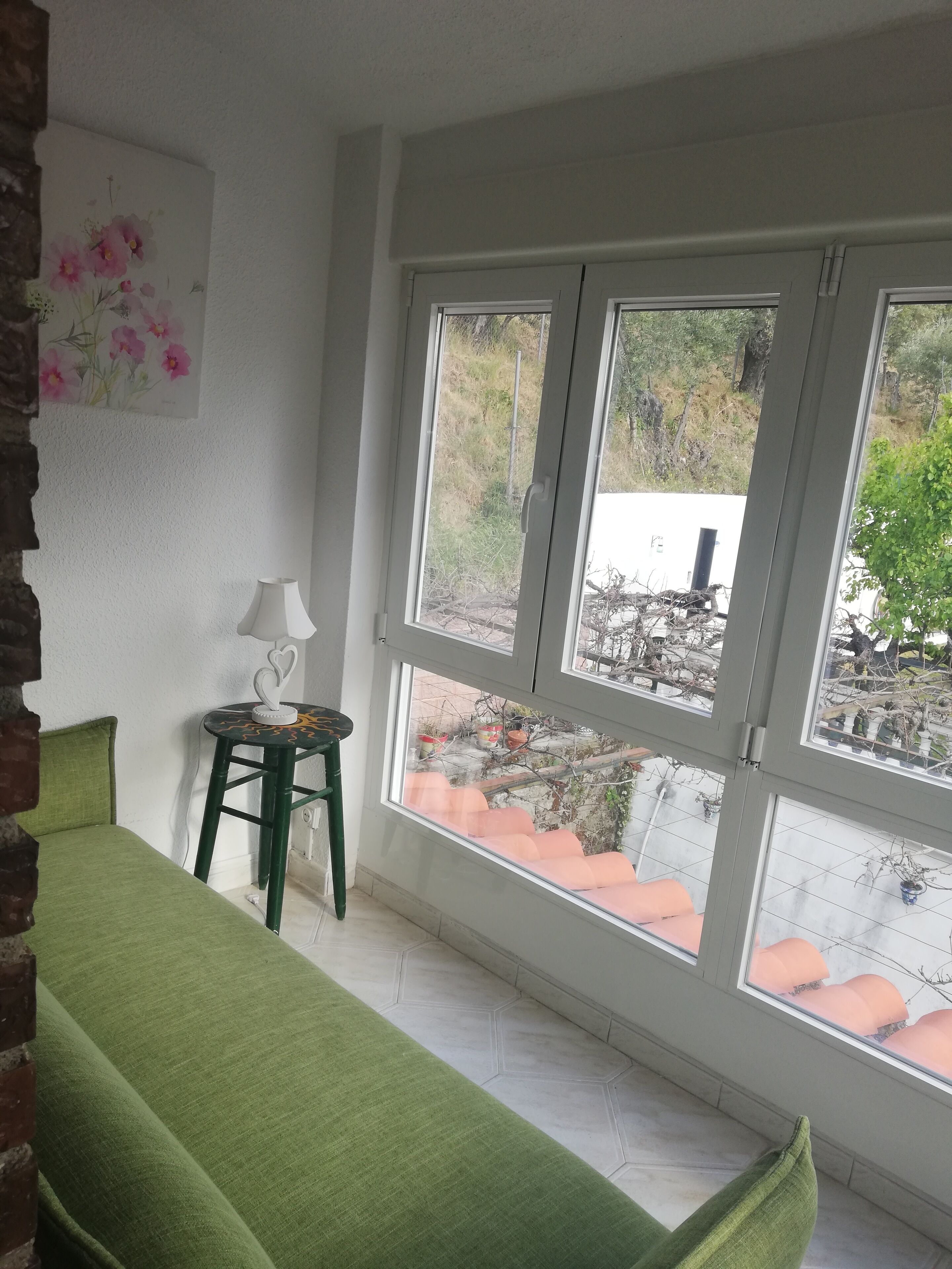 Et værelse med en grøn sofa, et lille bord med en lampe og et vindue med udsigt udad.