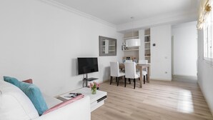 A modern living room with a white sofa, a flat-screen TV, and a dining area with white chairs and a wooden table. - El Viso Smart / Smart Apartments Madrid (Madrid)