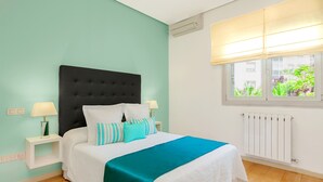A bedroom with a bed, two bedside tables with lamps, a window with a view of greenery, and a radiator. - El Viso Smart / Smart Apartments Madrid (Madrid)