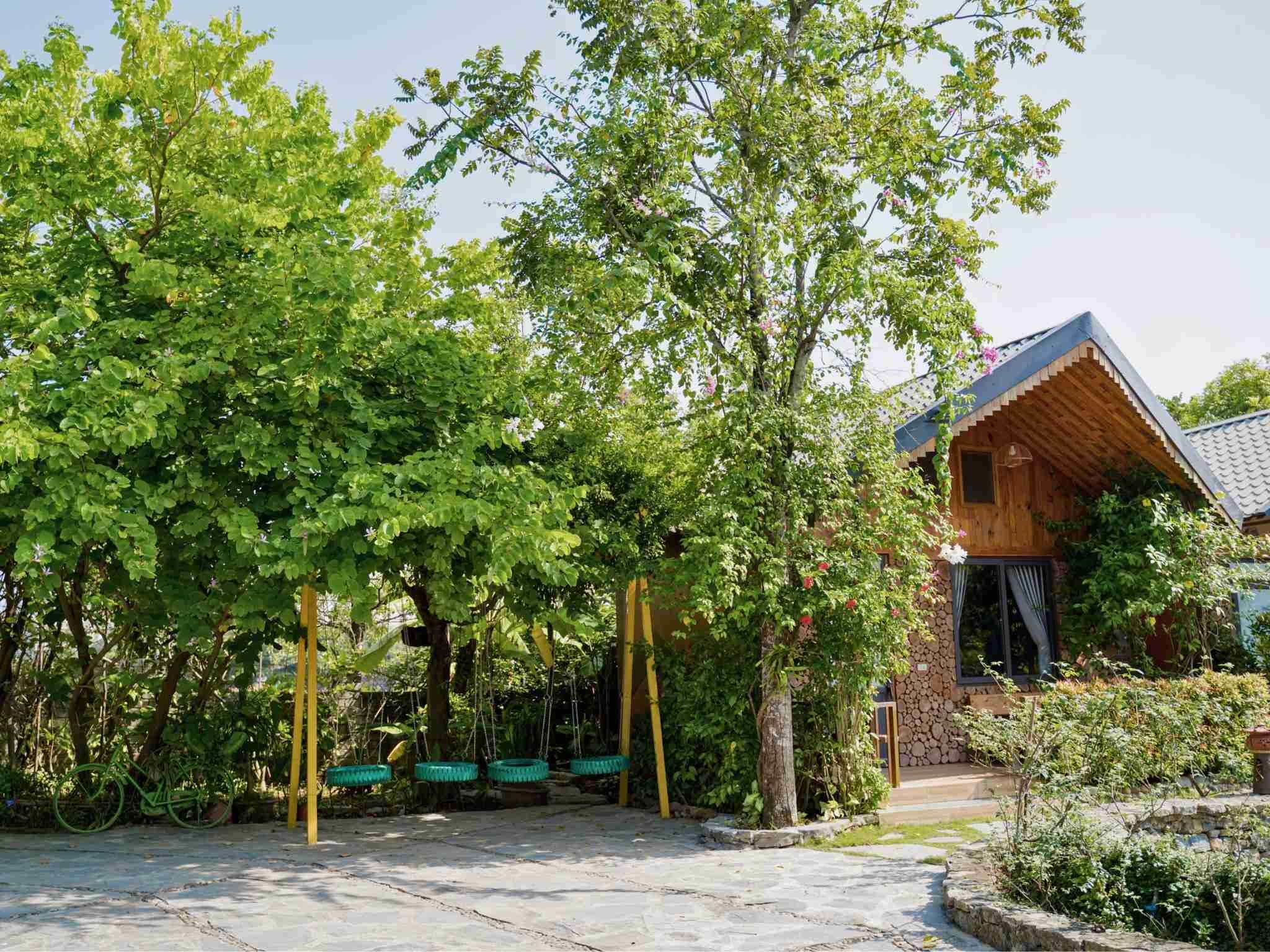A wooden building with a sloped roof, surrounded by lush greenery and a stone pathway.
