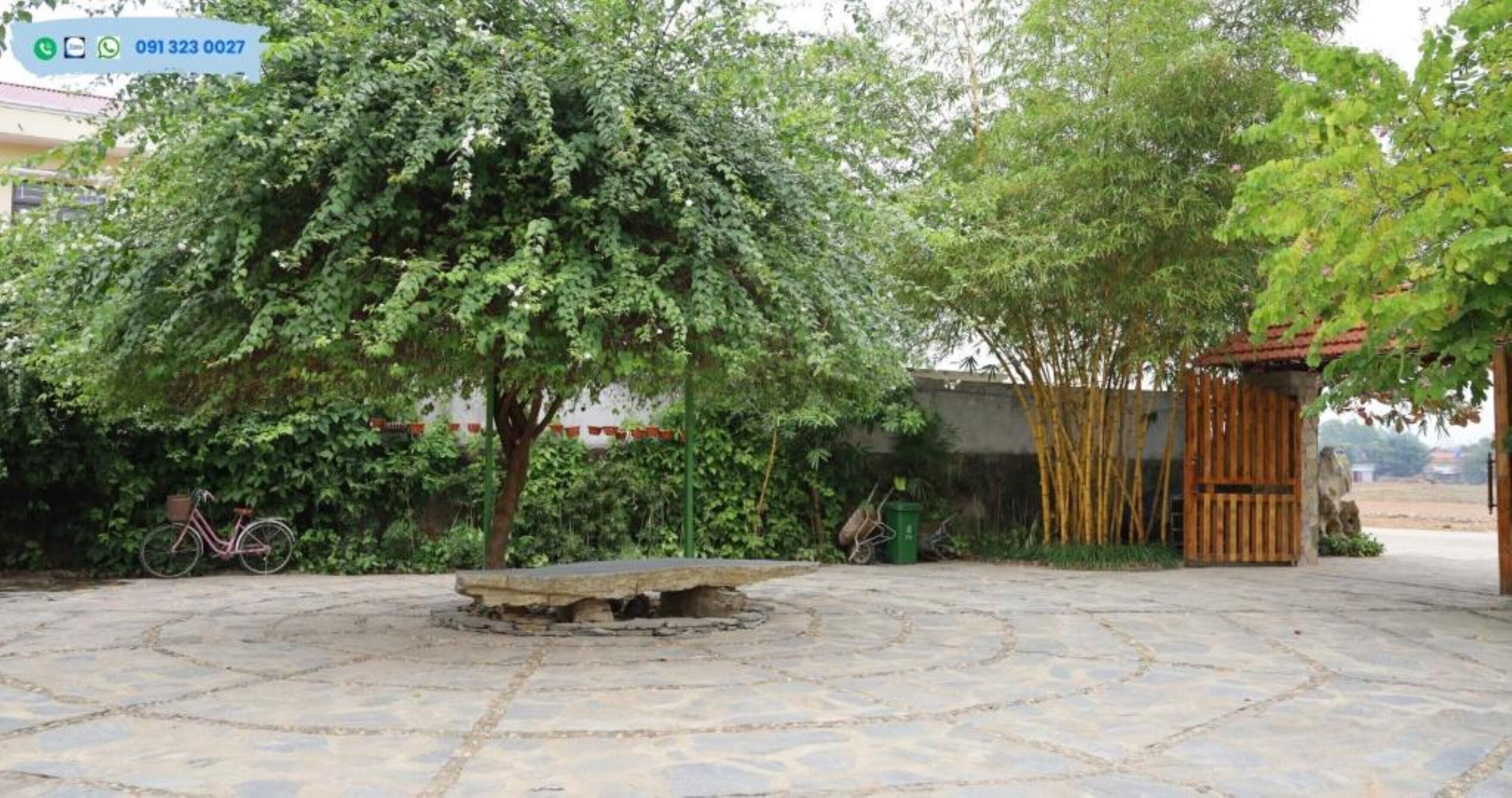 Un patio con un banco de piedra, una bicicleta y una cerca de bambú.