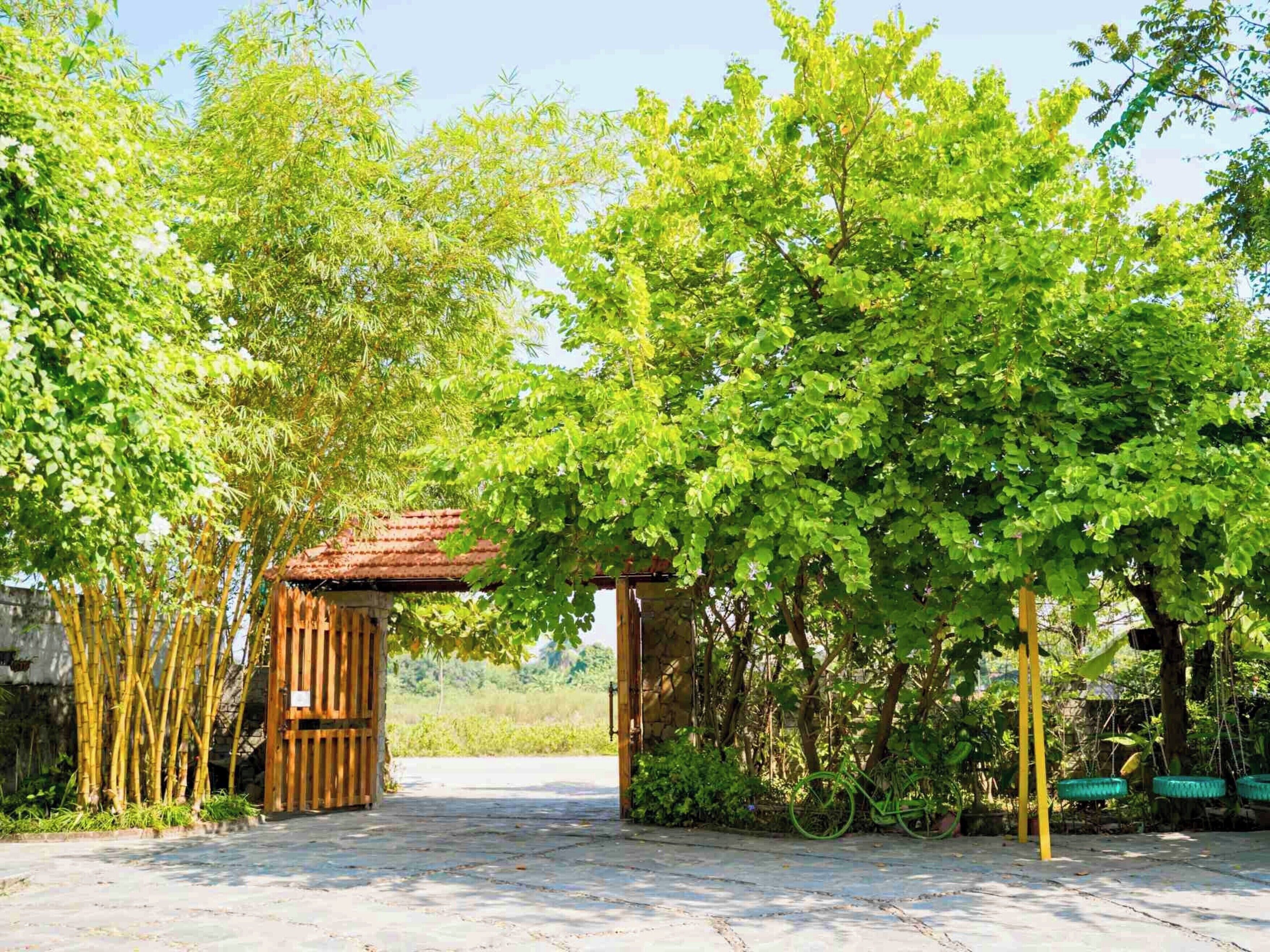 Un sendero de piedra conduce a un portón de madera rústico, rodeado de abundante vegetación y bambú.